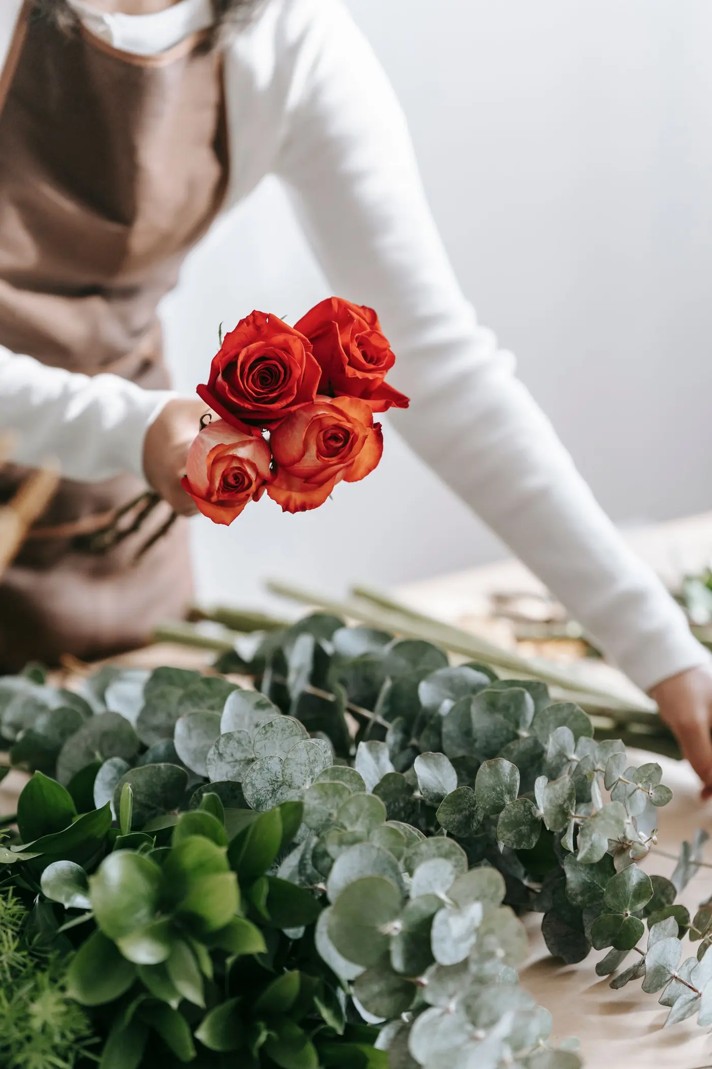 Une fleuriste compose un bouquet de roses et d'eucalyptus dans un atelier lumineux